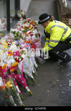 Un policier regarde des fleurs près de la scène à George Square, à Glasgow, où un camion-benne s'est écrasé sur un groupe de piétons qui a fait six morts. Banque D'Images