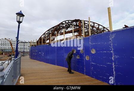 Un homme s'épare à travers une fenêtre d'observation sur Eastbourne Pier dans East Sussex, alors que les travaux continuent de démanteler la carcasse en acier de l'arcade de divertissement sur le quai classé Grade II qui a été laissé dévasté par un incendie plus tôt cet été. Banque D'Images