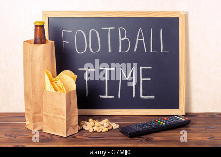 Les fans de football, concept de bouteille de bière dans le sac en papier brun, chips, pistaches, télécommande de la télévision et de l'écriture texte temps football Banque D'Images