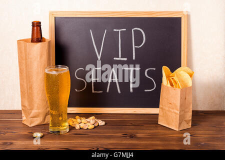 Les fans de football, concept de bouteille de bière dans le sac en papier brun, verre, chips, pistaches et texte de l'écriture à la craie écrit places VIP Banque D'Images