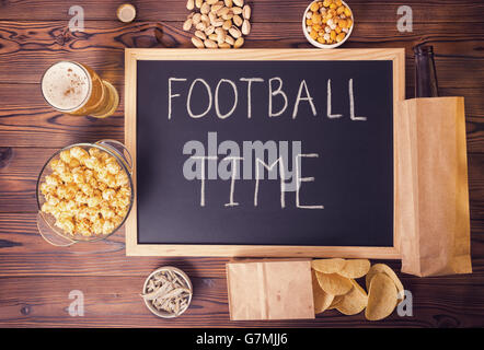 Les fans de football, concept de bouteille de bière dans le sac en papier brun, chips, pistaches et de l'écriture texte écrit en chalkbo temps football Banque D'Images