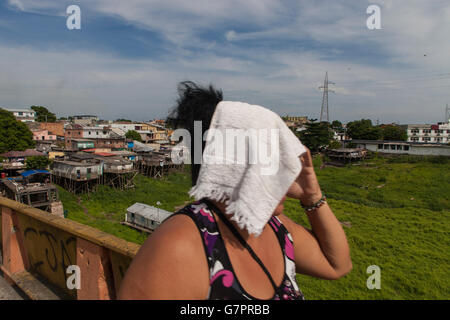 Femme couvre visage parce que de la chaleur sur une journée ensoleillée et humide à Manuas city - maisons sur pilotis à favela en arrière-plan, domaine où les inondations sont susceptibles de se produire, au Brésil. Banque D'Images