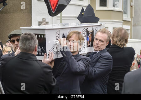 Le cercueil décoré par le visage de Steve Strange est tiré de la cheminée par des membres du Ballet de Spandau, dont Gary Kemp (deuxième à droite) et Steve Norman (avant à droite), et Boy George (à gauche) à l'extérieur de l'église All Saints, Porthcawl, au pays de Galles, où se déroulent les funérailles de la pop star des années 80. Banque D'Images