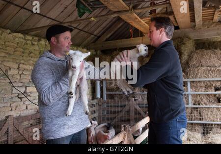 Le Premier ministre David Cameron (à droite) aide l'agriculteur Julian Tustian à nourrir les agneaux nouveau-nés à Dean Lane Farm, près de son domicile dans l'Oxfordshire, avant d'assister à un service du dimanche de Pâques avec sa femme Samantha. Banque D'Images