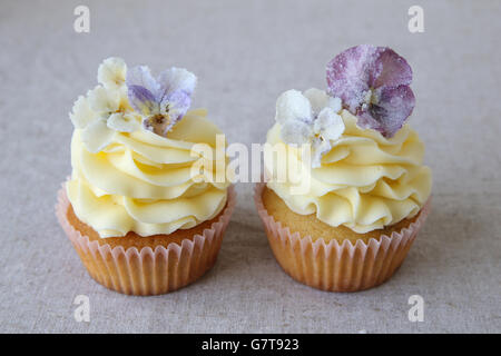 Cupcakes jaune violet avec des fleurs comestibles sucrées sur fond de lin Banque D'Images