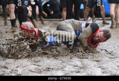 Les participants glissent et glissent dans la boue pendant le Tough Mudder London West à Culden Faw à Henley-on-Thames, Oxfordshire. Banque D'Images