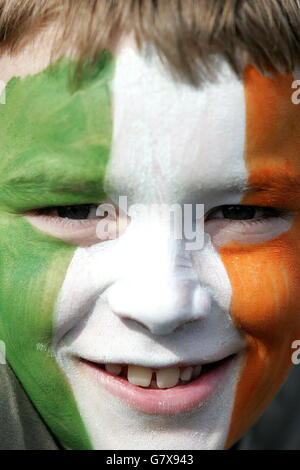 Un jeune gardien de festival entre dans l'esprit de la fête avec son visage peint dans les couleurs vert, blanc et or du drapeau irlandais. Banque D'Images