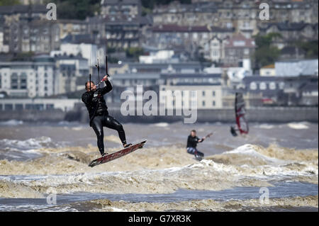 Un kitesurfer obtient un peu d'air sur des vagues molles, avec la station balnéaire de Weston-super-Mare en arrière-plan dans des conditions proches parfaites dans la mer, lors d'une chaude, ensoleillée et venteuse journée dans le canal de Bristol, Somerset. Banque D'Images