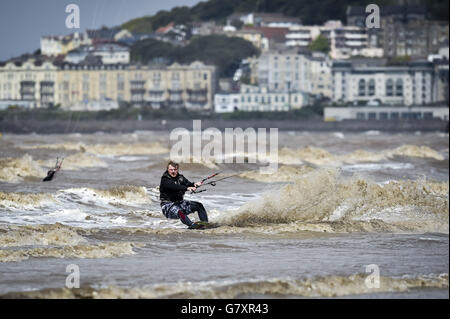 Un kitesurfer navigue sur des vagues molles, avec la station balnéaire de Weston-super-Mare en arrière-plan dans des conditions proches parfaites dans la mer, lors d'une chaude, ensoleillée et venteuse journée dans le Canal de Bristol, Somerset. Banque D'Images