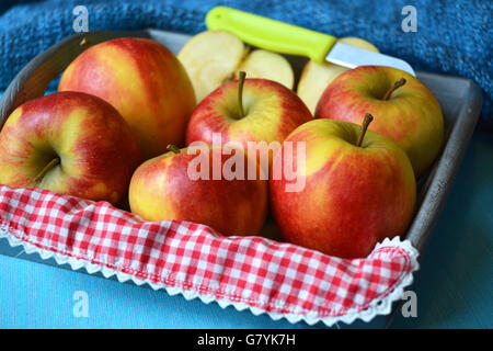 Close up de rouge, jaune, vert pommes dans bol en bois avec couteau et tranches de pomme rouge blanc campagne nostalgique napperon damier Banque D'Images