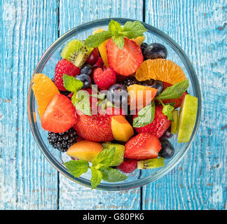 Salade de fruits frais avec divers genre de Berry et d'agrumes servi dans un bol en verre, placé sur la table en bois Banque D'Images