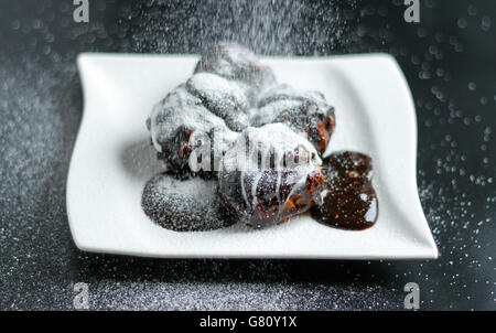 Profiterole pièces sur une plaque blanche recouverte de crème au chocolat et sucre en poudre Banque D'Images