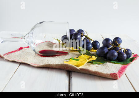 Installation rustique avec un verre de vin rouge sec, les raisins et les feuilles d'automne sur un tissu texturé Banque D'Images