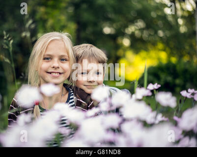 Belle fille blonde et adorable garçon de se cacher dans les fleurs Banque D'Images