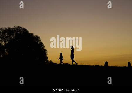 Garçon et Silhouette femme marche sur terrain contre ciel clair pendant le coucher du soleil Banque D'Images