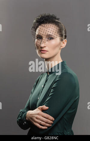 Portrait of woman avec net covering face contre l'arrière-plan gris Banque D'Images