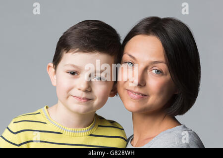 Portrait of smiling boy with mère contre l'arrière-plan gris Banque D'Images