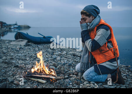 Vue latérale sur toute la longueur de teenage girl sitting par feu sur Lakeshore Banque D'Images