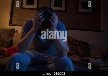 Vue avant du man with head in hands while sitting on sofa at home Banque D'Images