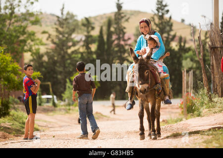 Une femme et son jeune enfant ride un âne vers le bas une route de terre dans le village de Ben Khili, Maroc. Banque D'Images