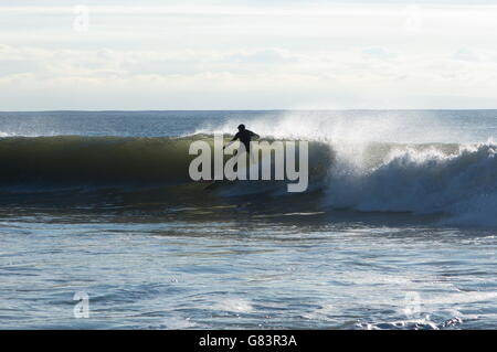 Surfer en silhouette par la lumière à travers l'onde courses la déferlante sur un point break au Pays de Galles. Le surf est un sport populaire pour les touristes. Banque D'Images