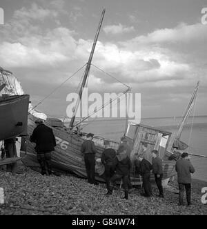 Aider aide à guider le petit bateau de pêche lorsqu'il est transporté par un treuil à essence sur la plage escarpée de Beer à Devon.Le village, qui abrite sous d'imposantes falaises de craie, est habituel comme centre de pêche car il n'a pas de véritable port ou de quai.Les bateaux sont limités à des tailles plus petites afin qu'ils puissent être transportés à terre avec une relative facilité. Banque D'Images