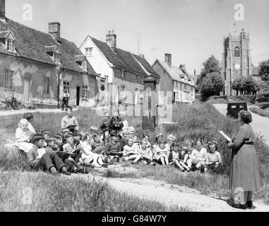 Les écoliers du village de Monks Eleigh dans le Suffolk ont une leçon au soleil sur le vert du village, à côté de la pompe de village longtemps désutilisée. Banque D'Images