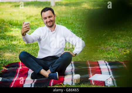 Photo de beau gars sympa en plein air au matin. Jeune homme souriant et décisions sur téléphone mobile photo selfies avec expressions cool Banque D'Images