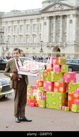 M. Bean, joué par Rowan Atkinson, célèbre le 25e anniversaire du personnage sur le Mall, en face de Buckingham Palace, Londres, avec un gâteau et son ours en peluche. Banque D'Images
