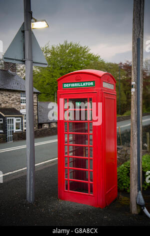 Une boîte de téléphone rouge vif convertie en chambre d'urgence et défibrillateur en cas de crises cardiaques , sur le bord de la route en Cwrt village, Parc National de Snowdonia, Gwynedd, au nord du Pays de Galles UK Banque D'Images