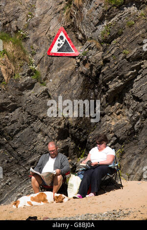 Royaume-uni, Pays de Galles, Ceredigion, Llangrannog, amusantes, des signes de base assis à quelques falaises ignorant la chute de rochers danger sign Banque D'Images