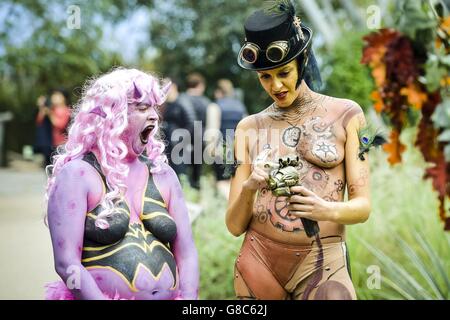 Un modèle nawns tandis qu'un autre vérifie son arme alors qu'ils attendent de défilé à l'intérieur du Biome méditerranéen pendant le festival international de peinture de corps de BodyFactory deux jours au projet Eden, Cornwall. Banque D'Images