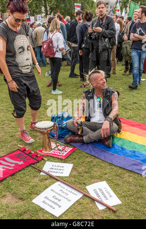 Un partisan de Jeremy Corbyn reposant sur un drapeau arc-en-ciel sur l'herbe entourée par des déclarations soutenant le leader en place du Parlement , , Londres. Banque D'Images