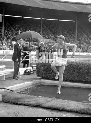 Maurice Herriott (Sparkhill Harriers) sur le point d'entrer dans le saut d'eau pendant le Steeplechase au stade White City, Londres. Il représentera l'Angleterre aux Jeux du Commonwealth à Kingston, en Jamaïque. Banque D'Images