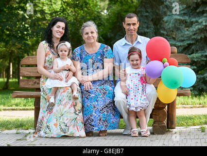 Grande famille s'asseoir sur le banc de bois du parc de la ville, saison d'été, enfant, parent et grand-mère, petit groupe de cinq personnes avec ballo Banque D'Images