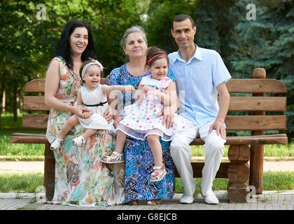 Grande famille s'asseoir sur le banc de bois du parc de la ville, saison d'été, enfant, parent et grand-mère, petit groupe de cinq personnes Banque D'Images