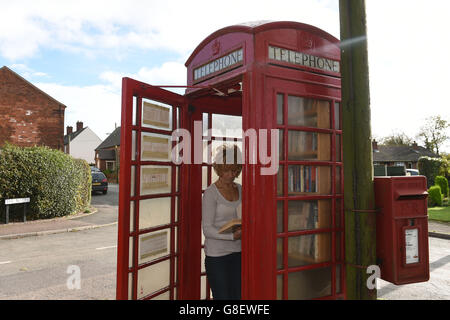 Wendy Hanlon regarde des livres dans une boîte téléphonique rouge qui a été convertie en une minuscule bibliothèque libre d'utilisation dans le village de Wall, dans le Staffordshire. Banque D'Images