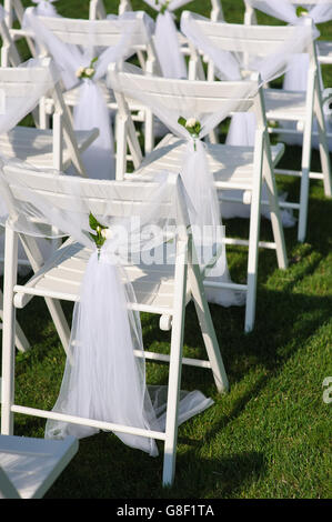 La décoration blanche chaises sur une pelouse verte. Des chaises disposés en rangées pour la cérémonie de mariage. Elles sont décorées pour les fêtes de fin d'événement. Banque D'Images