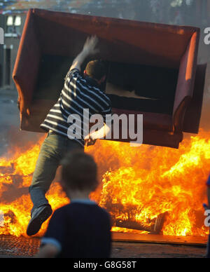 Un enfant jette du bois sur un feu de camp à Belfast. Dans toute l'Irlande du Nord, des centaines de feux de camp seront mis à feu, signalant le début de la plus grande journée de marche dans le calendrier de la commande Orange. Demain, des milliers d'Orangemen partiront dans les rues pour les défilés commémoratifs de la bataille de Boyne. La police et les troupes seront en attente dans le nord de Belfast, où les marcheurs traverseront le district d'Ardoyne à deux reprises. Banque D'Images