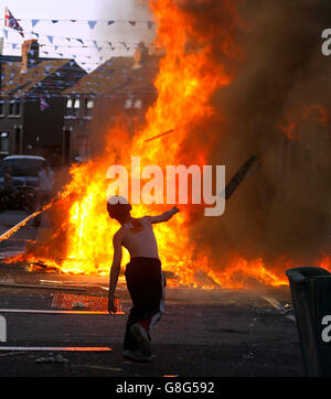 Un enfant jette du bois sur un feu de camp à Belfast. Dans toute l'Irlande du Nord, des centaines de feux de camp seront mis à feu, signalant le début de la plus grande journée de marche dans le calendrier de la commande Orange. Demain, des milliers d'Orangemen partiront dans les rues pour les défilés commémoratifs de la bataille de Boyne. La police et les troupes seront en attente dans le nord de Belfast, où les marcheurs traverseront le district d'Ardoyne à deux reprises. Banque D'Images