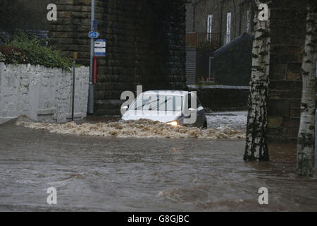 Une voiture traverse les eaux d'inondation à Mytholmroyd à Caldernon, dans le West Yorkshire, où les sirènes d'inondation ont été sondées après des détrots torrentiels. Banque D'Images