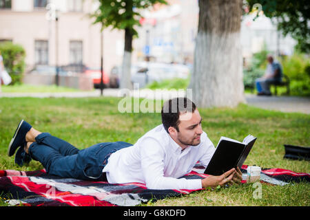 Beau jeune businessman reading book lying in the park Banque D'Images