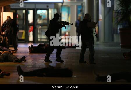 Les personnes jouant le rôle des hommes armés 'feu ouvert' à un arrêt de bus emballé pendant un exercice d'entraînement pour tester la réponse des services d'urgence à une attaque à armes à feu majeure au centre commercial Intu Braehead près de Glasgow. Banque D'Images