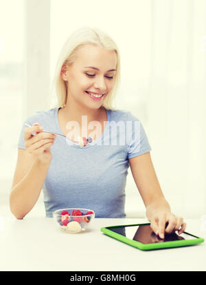 Smiling woman eating fruits avec tablet pc at home