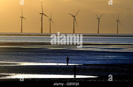 Le soleil se couche sur les éoliennes qui peuvent être vues de la plage de Crosby, Merseyside alors que deux des Iron Men d'Antony Gormley regardent la mer. Banque D'Images