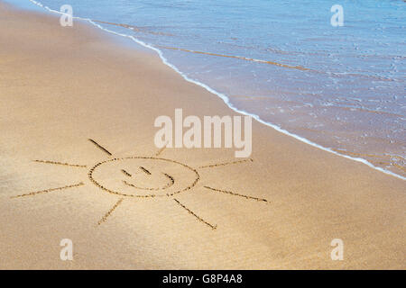 Smiley soleil de face dessin sur une plage. UK Banque D'Images