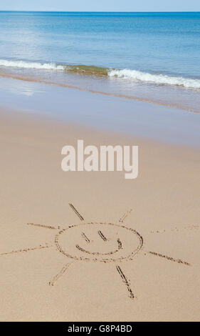 Smiley soleil de face dessin sur une plage. UK Banque D'Images