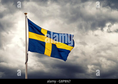 De brandir le drapeau national suédois sur jour de vent froid, sombre nuages orageux en arrière-plan Banque D'Images