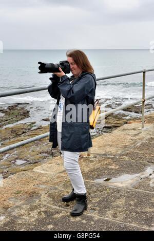 Une femme photographe en utilisant votre appareil photo reflex numérique avec un objectif zoom téléobjectif Porthleven dans Cornwall England UK Banque D'Images