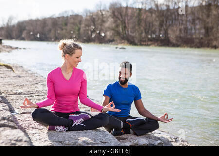 Jeune couple practicing yoga par le Riverside Banque D'Images